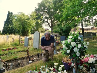Elderly Man kneeling at a graveside grieving and remembering a loved one a warm day