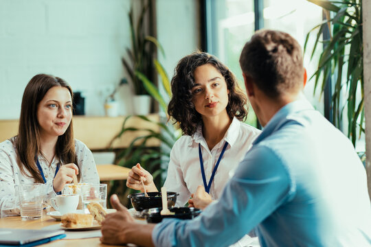 Three young coworkers chatting over healthy lunch in bright office cafeteria