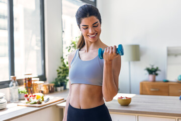 Beautiful sporty woman working out with weights in the kitchen at home