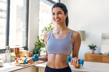 Beautiful sporty woman working out with weights in the kitchen at home