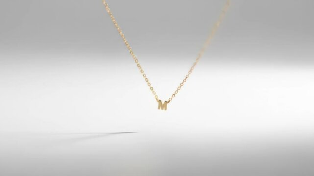 Elegant golden necklace with letter M pendant on white background, a jewelry fashion accessory.