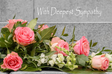 Condolence card with text: With Deepest Sympathy. Funeral floral arrangement of red roses. Memorial site at Hietaniemi cemetery in Helsinki, Finland. Beautiful funeral flowers on the stone steps.