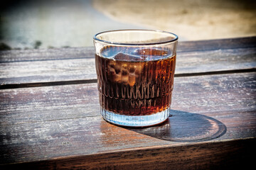 A refreshing iced rum drink sits on a weathered wooden table, waiting for someone to enjoy a moment of relaxation in the sun.