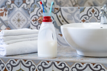 A clean bathroom countertop features a bottle of detergent, neatly folded white towels, and a bowl. The decor combines stylish tiles and a fresh atmosphere.
