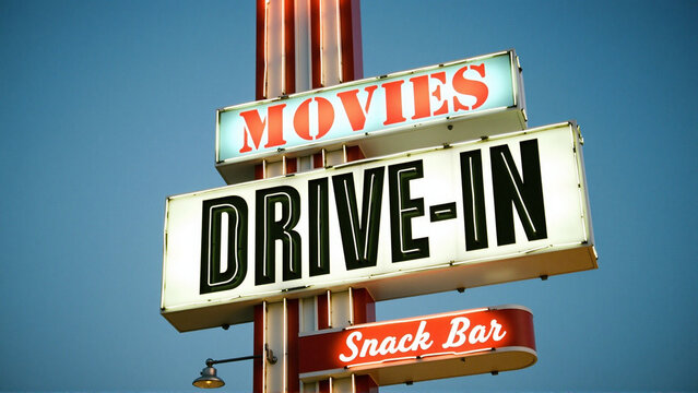 A movie theater sign with the words drive-in and "Movies" on it. - Powered by Adobe