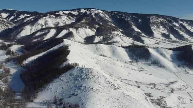 Drone footage of snowy mountains, valleys, and forests in Ust-Koksa, Altai Republic, Russia, under clear skies, showing the remote region&rsquo;s beauty during winter.