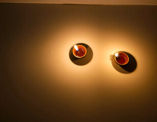 Two clay Diya lamps casting warm light on wall