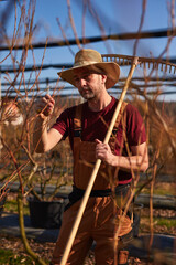 Male gardener with hat working with a rake in a blueberries organic farm.