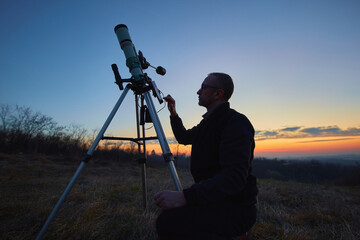 Amateur astronomer using telescope and smartphone for watching stars, Moon, planets and other celestial objects from a field in nature.