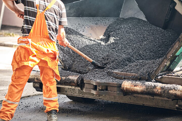 Construction workers working on a new asphalt layer on a public street.
