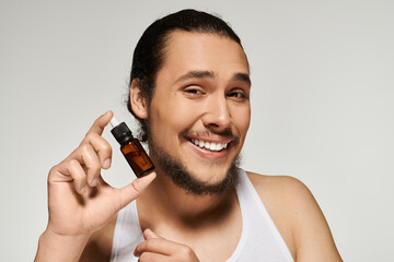 Smiling young man showcases essential oil bottle with confidence and charm in bright setting