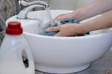 Water pours from a faucet as hands scrub a cloth in a stylish white sink. The light-filled laundry...