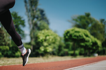 Close-up of a runner wearing athletic shoes moving forward on a track in a lush park setting. The...