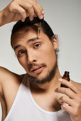 Handsome young man applying beard oil in a modern indoor setting with a serene expression