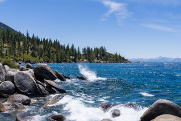 Lake Tahoe, California, USA, high winds creating waves splashing against the rocks, blue sky and...