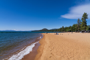 Beach at South Lake Tahoe, California, USA, deep blue sky and clear waters, mountains in the background. People tanning and bathing