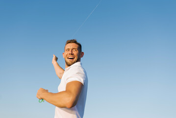Smiling Man Flying Kite Against Blue Sky