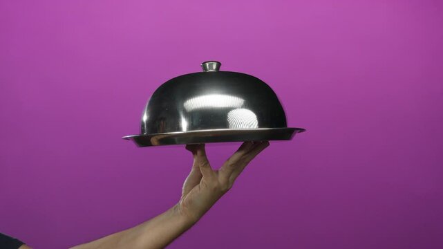 Man holding silver serving tray against bold pink wall, showcasing elegance in a minimalist isolated setting, emphasizing hand and metallic surface.