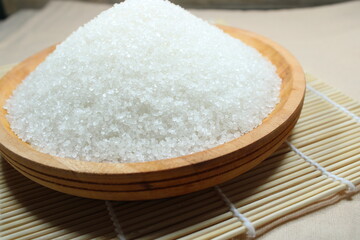 A wooden bowl filled with white crystal sugar placed on a bamboo mat