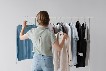 Woman choosing clothes in a store, shopping concept. Closeup of young girl choose clothing over gray wall background with copy space.