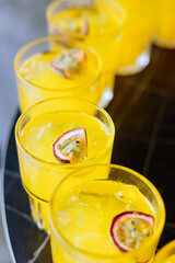 Close-up of vibrant yellow cocktails with passion fruit garnish, served on a tray at a party or summer event.
