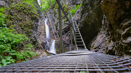 Steel grating walkway and stairs leading up alongside a waterfall cascading down a rocky cliff in a...