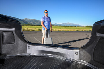 Tourist is putting luggage in car trunk at airport parking lot, ready for road trip adventure