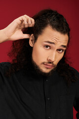 Young bearded man showing off his stylish hair against a vibrant red backdrop