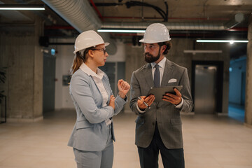 Architect and engineer discussing building plans using tablet in unfinished building