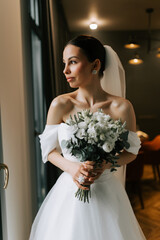 Beautiful bride with bouquet poses gracefully in modern indoor setting before wedding ceremony