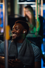 Smiling young man wearing earbuds and towel riding bus at night