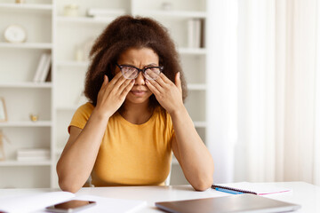 Tired young black woman rubbing her eyes with glasses on, feeling eye strain after prolonged screen...