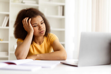 Bored young black woman resting her head on hand while staring at laptop. Tired of screen time or...