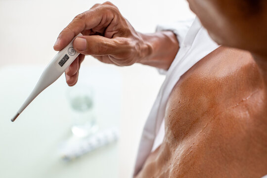 Man holding a digital thermometer showing a high temperature, indicating fever and self-care at home.