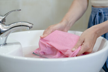Close-up of persons hands soaking pink cloth in sink. The setting a bathroom with simple decor. Concept of daily stains on clothes