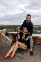 Stylish Romantic Couple Sitting on Rooftop Embracing Each Other with Cityscape and Forest in Background — Urban Love and Fashion Concept