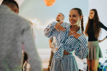 A cheerful group celebrates a birthday at home, featuring a joyful young woman in a striped outfit gesturing festively.