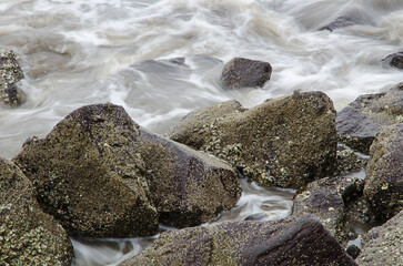 Waves crashing over the beach rocks, rocks and ocean with blurred motion of waves, rocky shoreline meeting coastal waters