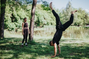 Two individuals engaging in exercise and gymnastics in a lush outdoor park setting, focusing on balance and wellness. The scene captures an active and energetic atmosphere surrounded by green nature.