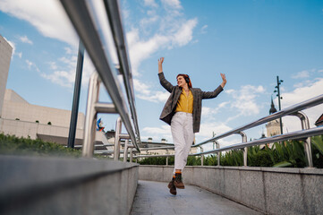 Young stylish woman listening music with headphones and dancing in the city