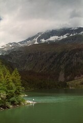 Man standing in clearing by lake with snowy mountains in misty background