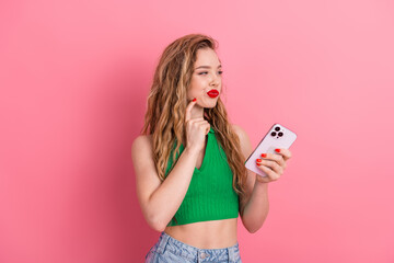 Charming young woman with a smartphone playfully gesturing against a pink background, showcasing...