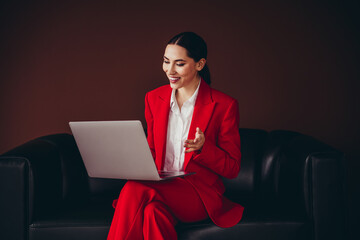 Confident Professional Woman in Red Suit Conducting Business on Laptop in Modern Setting