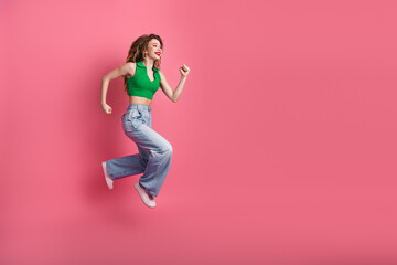 Joyful young woman jumping with excitement in vibrant casual outfit against a colorful pink...