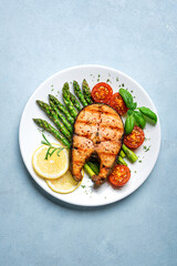 Grilled salmon steak with green asparagus, tomatoes and lemon slices