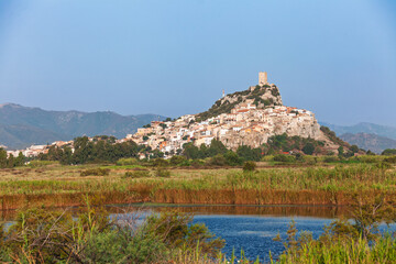 Hill town of Posada with historic tower overlooking lush wetlands in Sardinia Italy