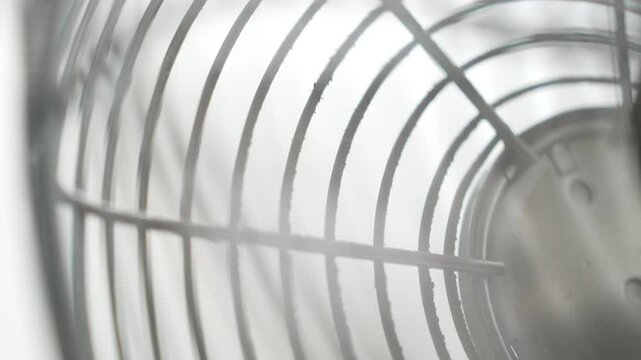 Close-up View of a Continuously Spinning and Oscillating Electric Fan's Dusty Metal Grille and Blades, Captured with a Shallow Depth of Field and Prominent Bokeh