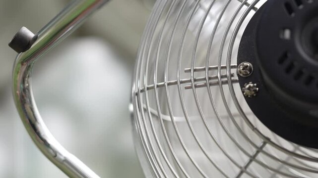 Close-up View of a Clean, Continuously Spinning Electric Fan, Showcasing its Polished Chrome Grille, Rapidly Rotating Blades, and Sleek Black Housing with Visible Screws