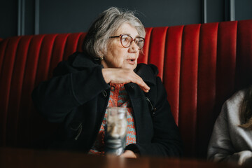 A senior woman engaging in an animated discussion while seated in a chic cafe booth with red...
