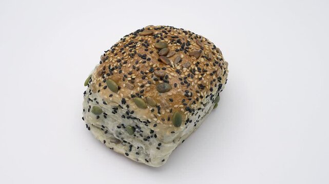 Rotating top-down shot of soft multigrain bread on white background, highlighting its seeded crust